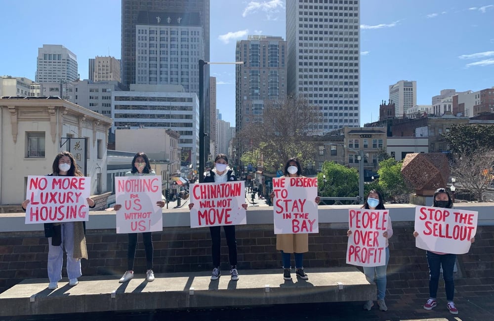 Six SF residents stand together in Chinatown with signs calling for housing justice and an end to displacement.