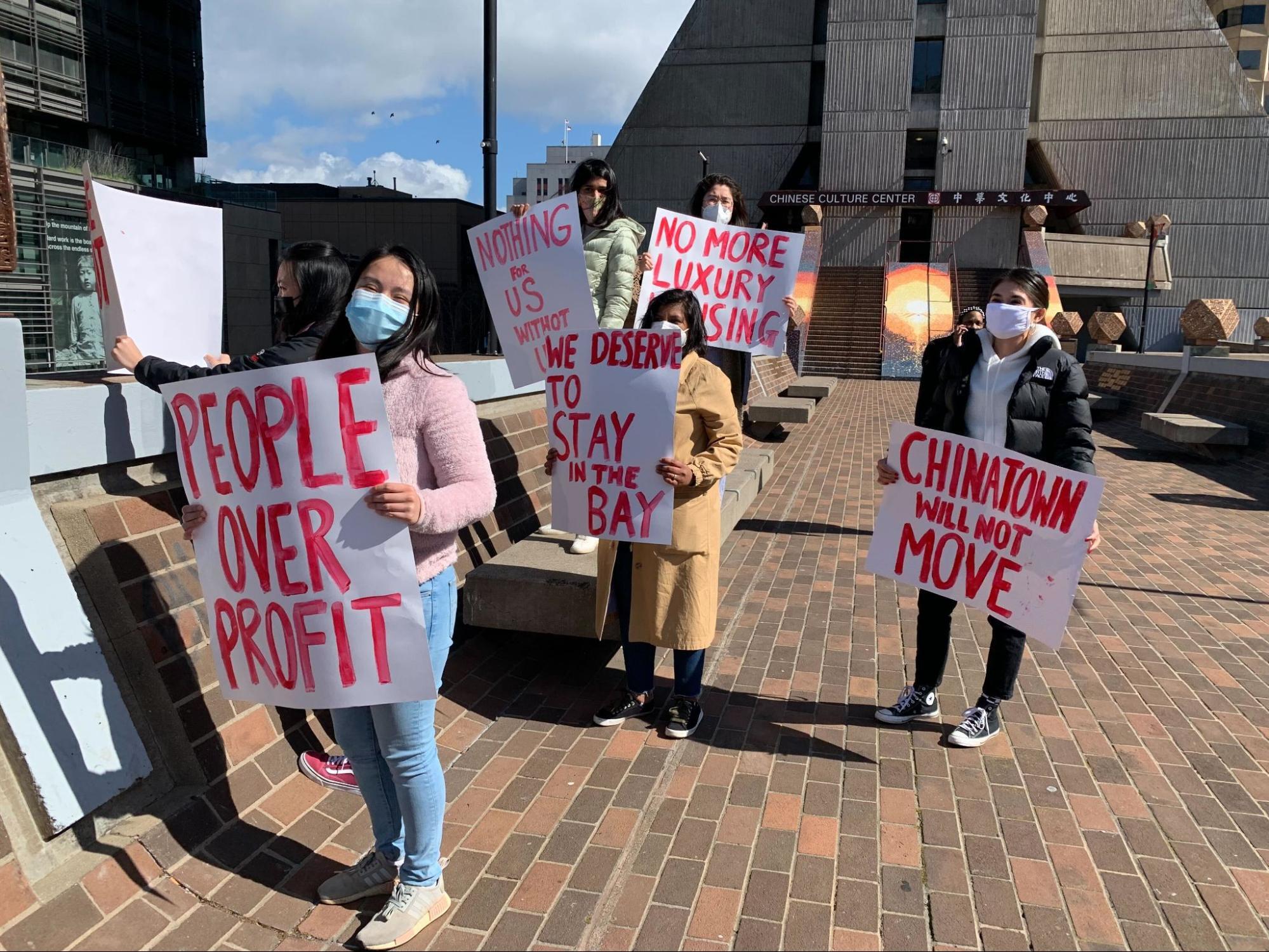 SF residents in Chinatown hold signs that read various messages like "people over profit" and "we deserve to stay in the Bay"