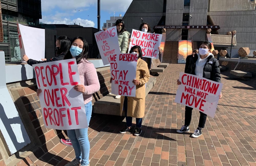 SF residents in Chinatown hold signs that read various messages like "people over profit" and "we deserve to stay in the Bay"