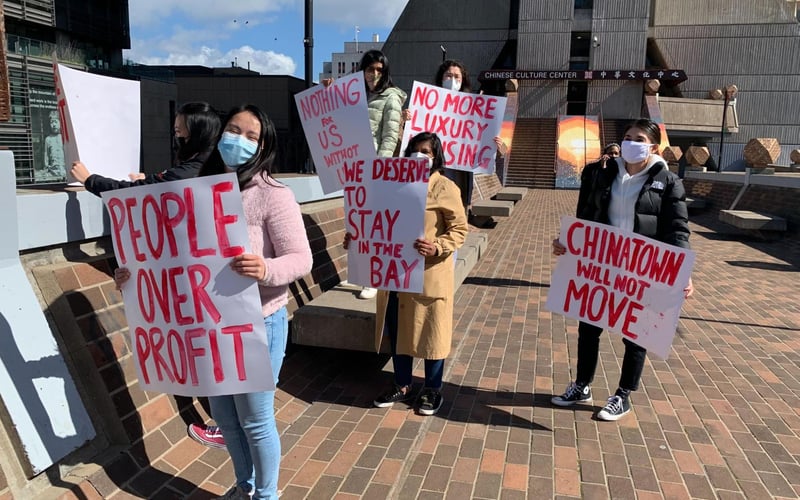 SF residents in Chinatown hold signs that read various messages like "people over profit" and "we deserve to stay in the Bay"