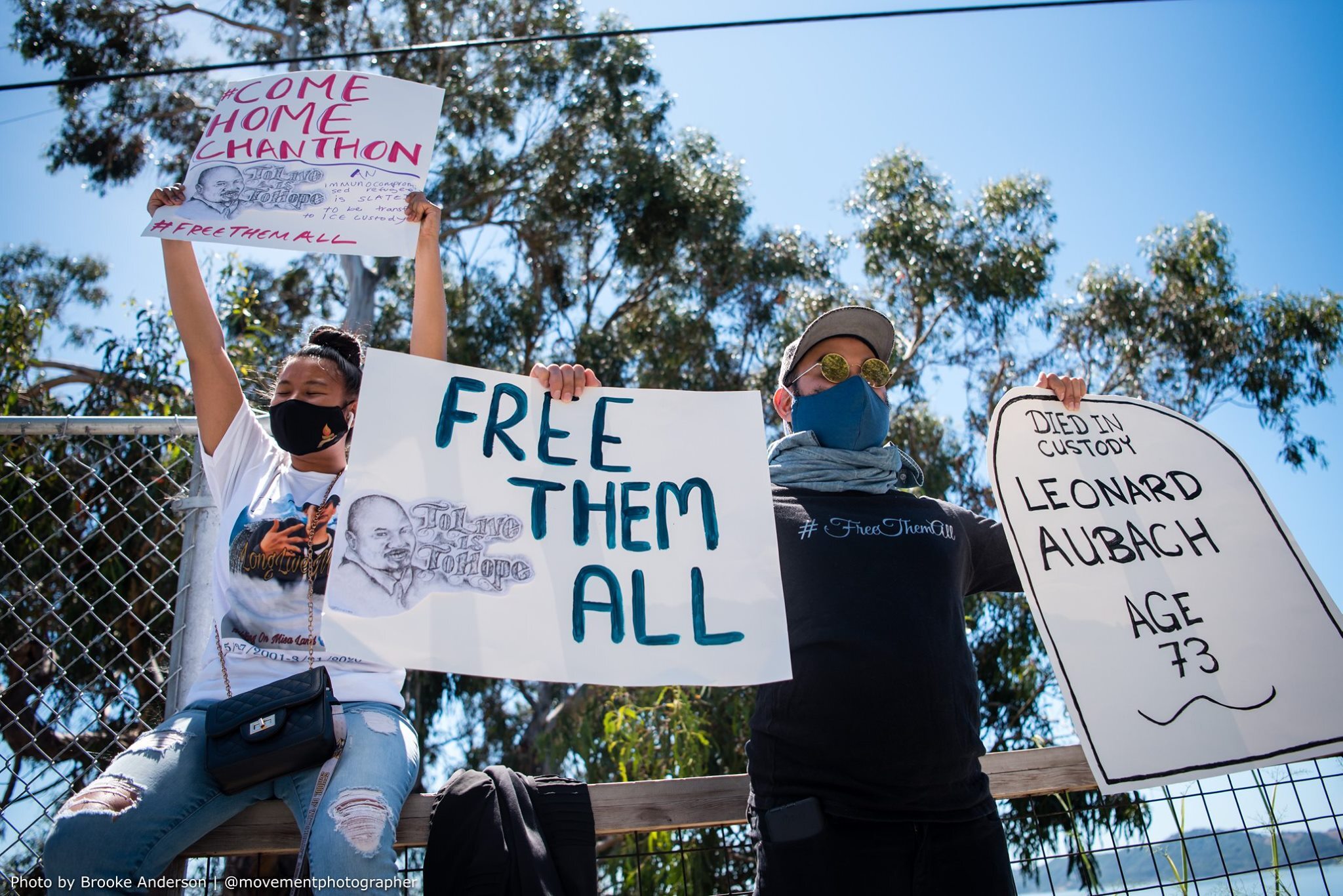 Two people wearing masks and holding signs that read "Free Them All"