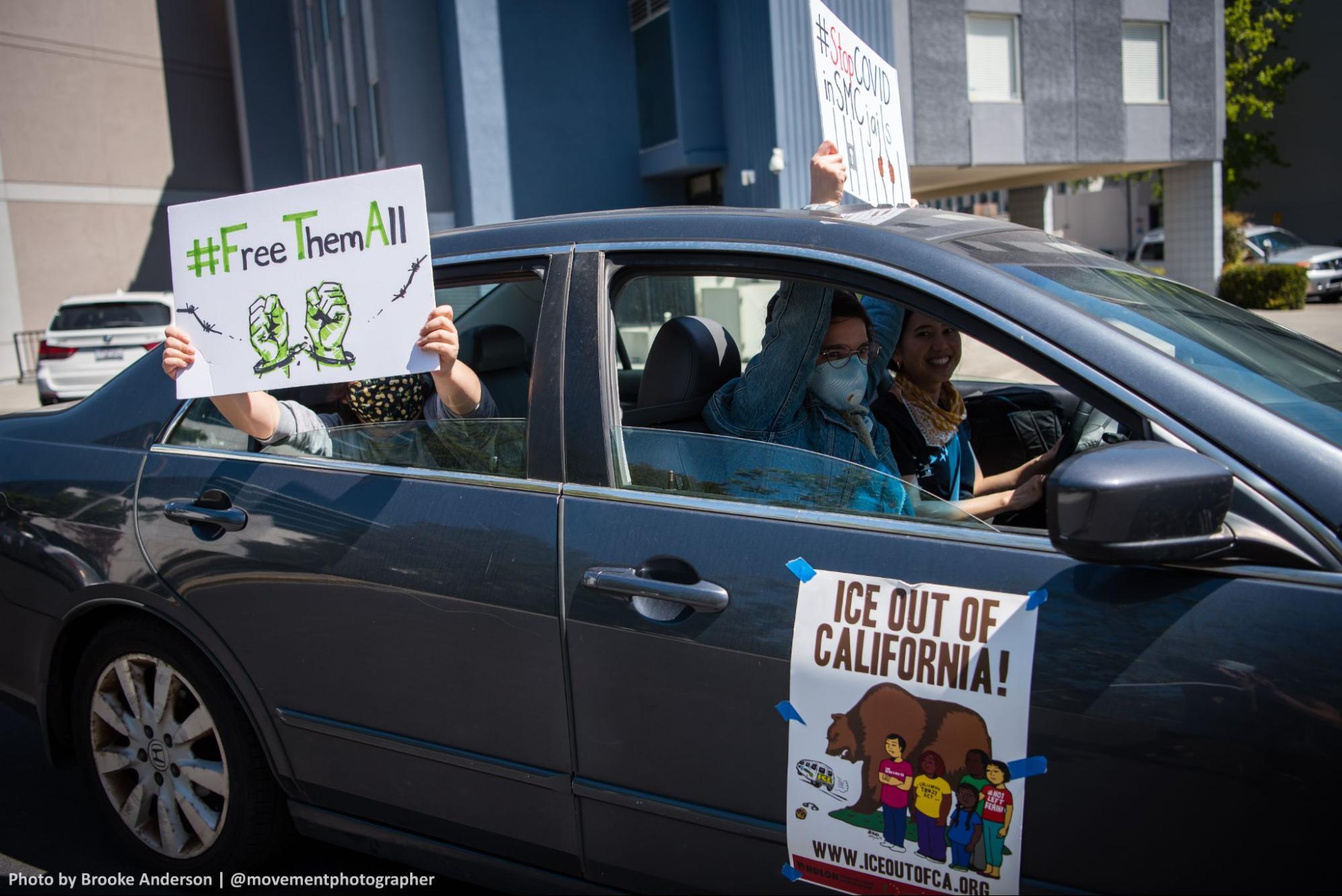 Community members in a car hold out "ICE out of CA" signs during a VISION car rally.