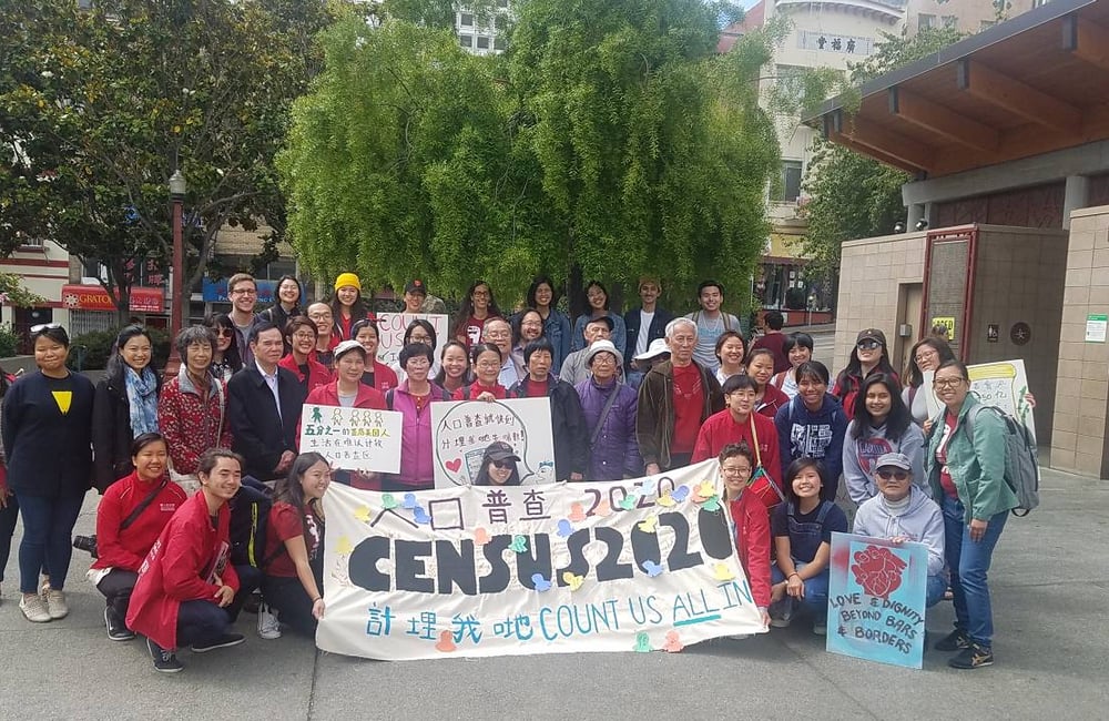 Dozens of San Francisco residents and advocates gather together behind a sign that says "Census 2020"