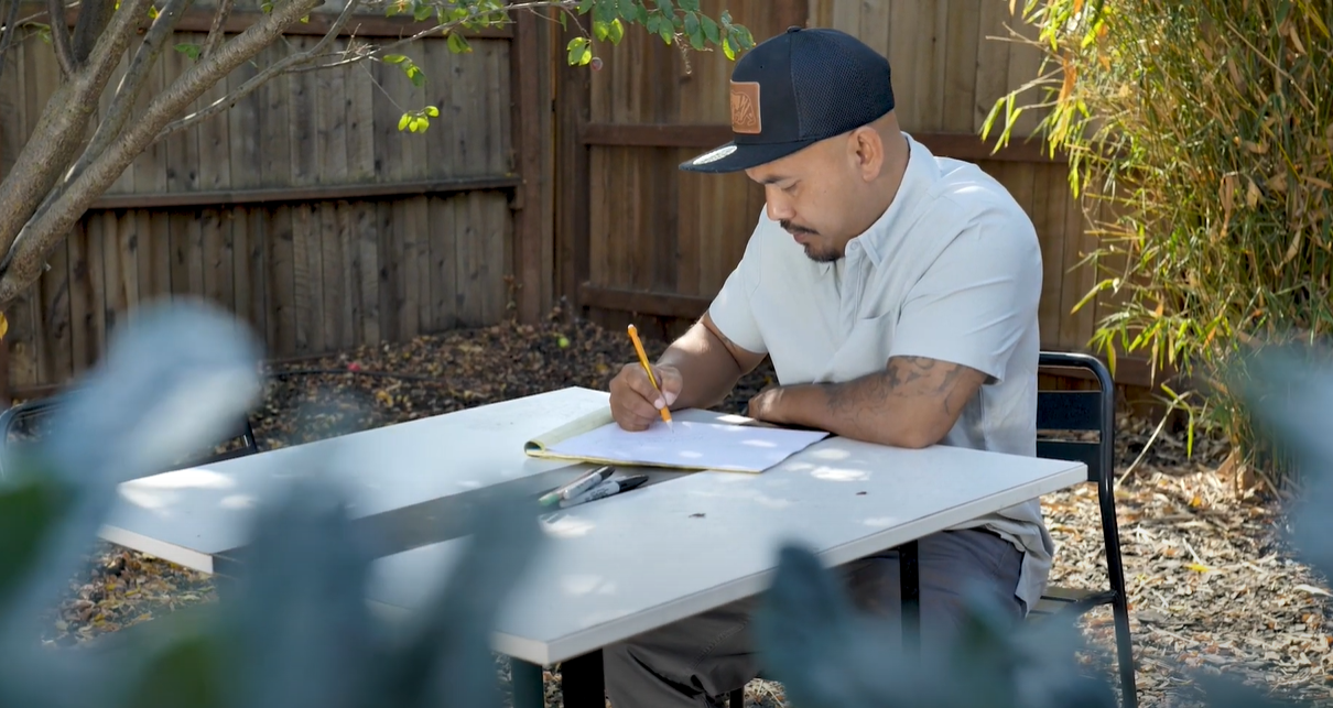 Bun, wearing a blue cap, sits on a table outdoors and draws.
