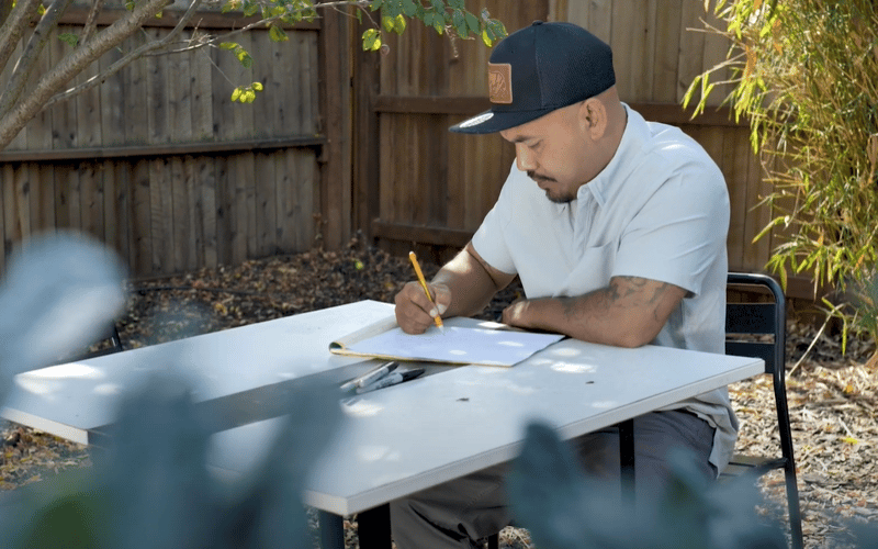 Bun, wearing a blue cap, sits on a table outdoors and draws.