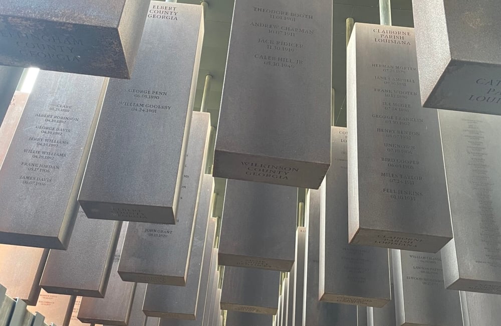 Large silver rectangle blocks hang from the ceiling in the National Memorial for Peace and Justice, with names of lynching victims memorialized on them.