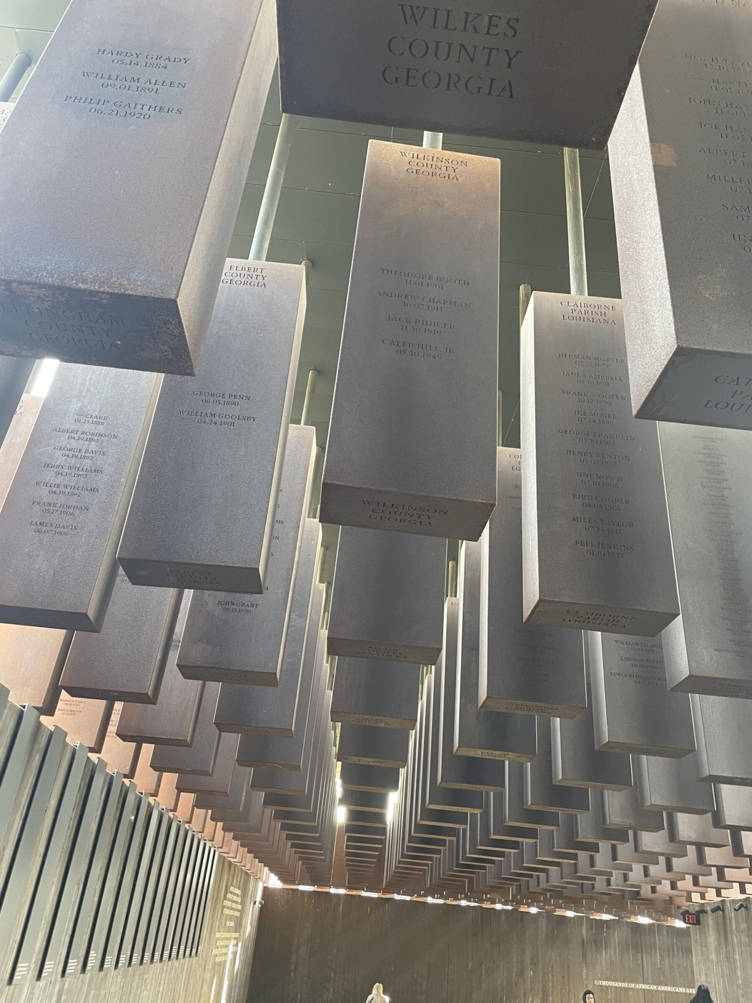 Large silver rectangle blocks hang from the ceiling in the National Memorial for Peace and Justice, with names of lynching victims memorialized on them.