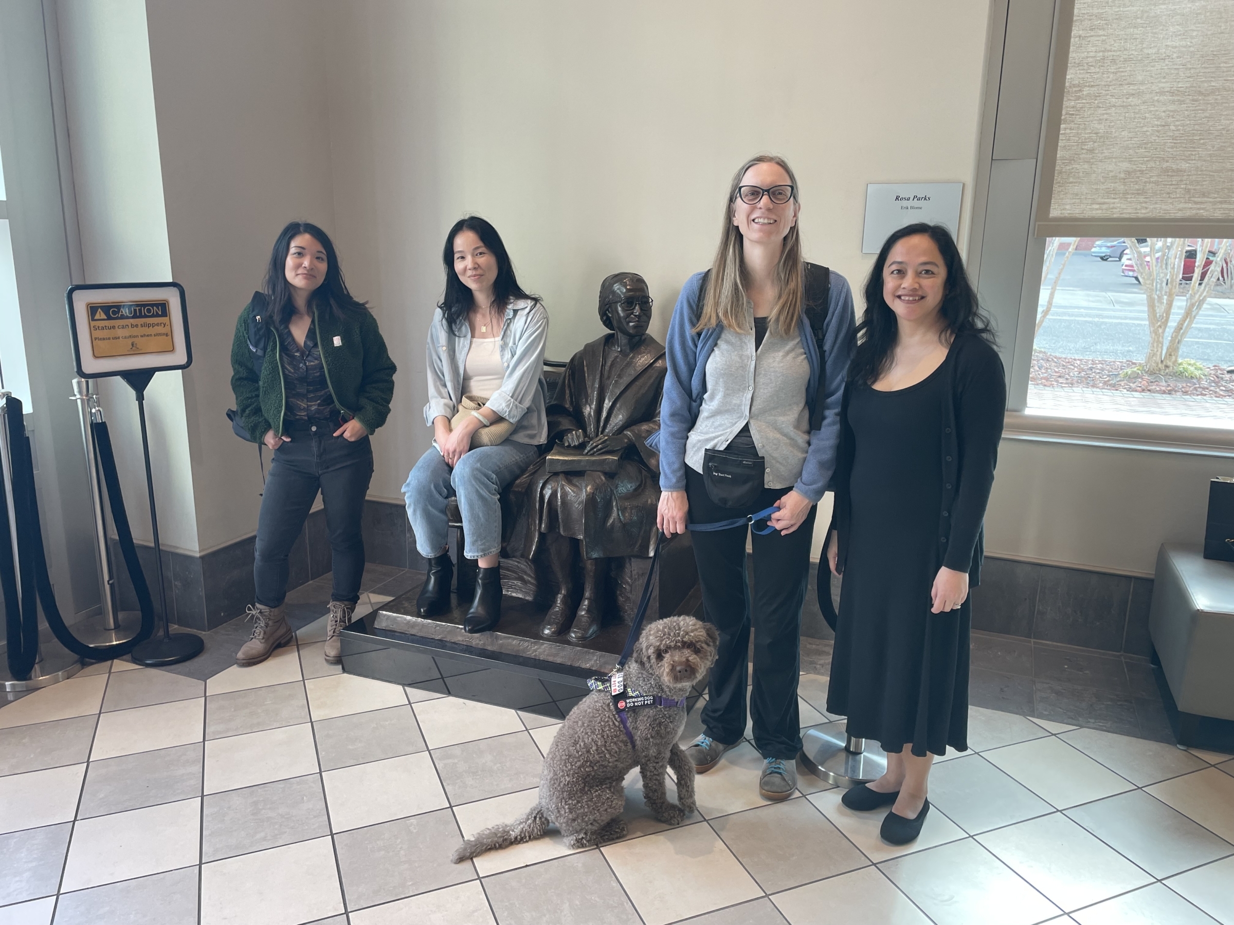 Four staff members stand by a statue of a seated Rosa Parks in the Rosa Parks Museum.