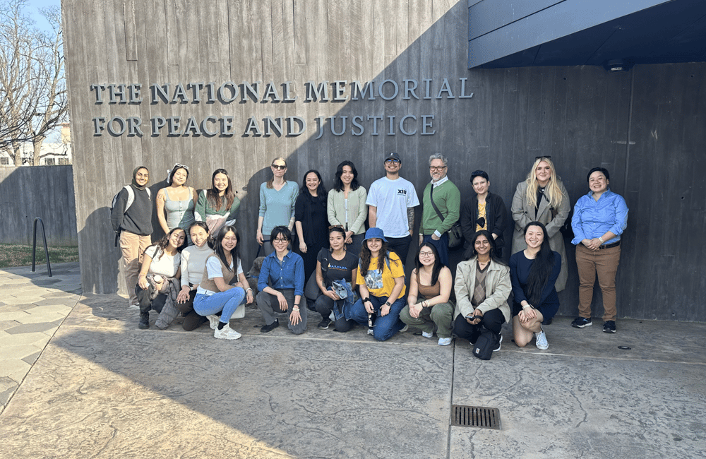 20 ALC staff members gather in a group photo under a sign that reads, "National Memorial for Peace and Justice"