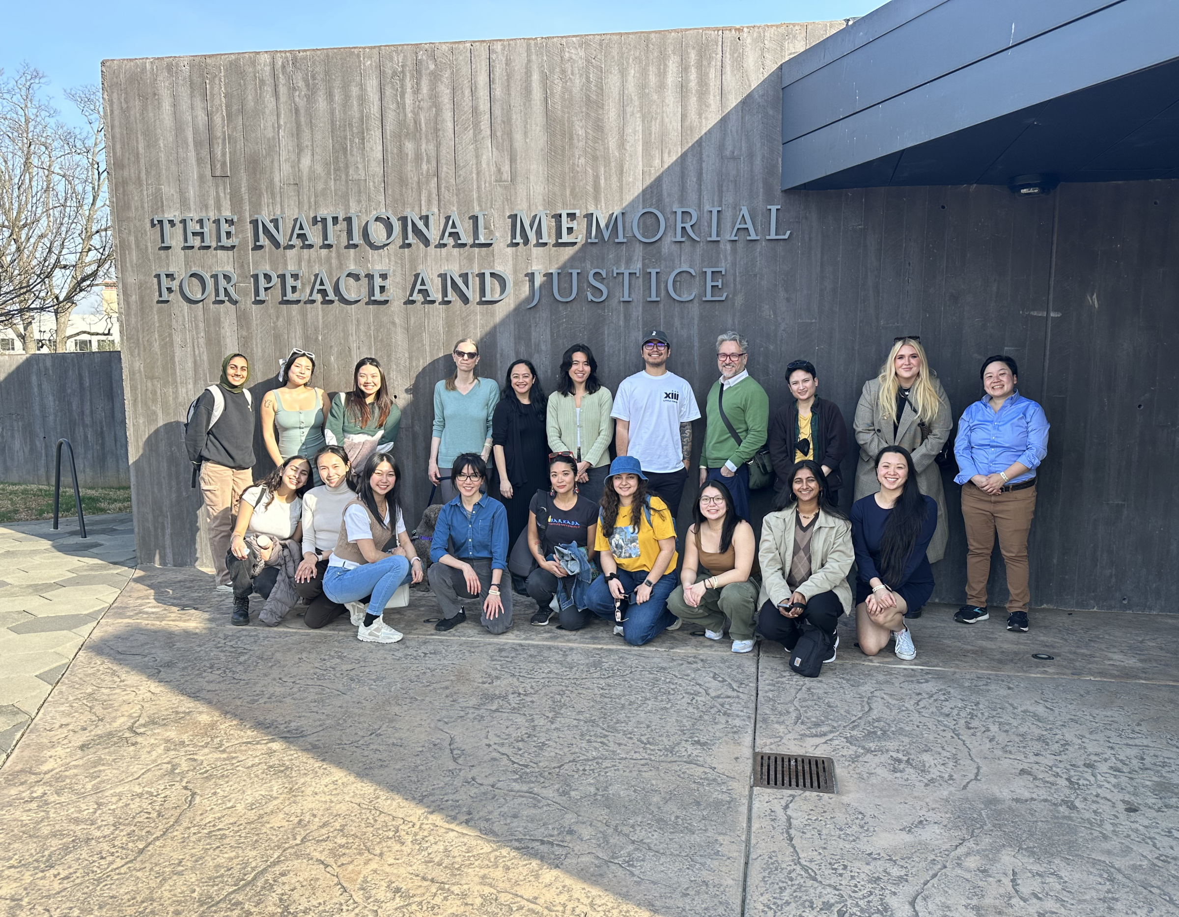 20 ALC staff members gather in a group photo under a sign that reads, "National Memorial for Peace and Justice"