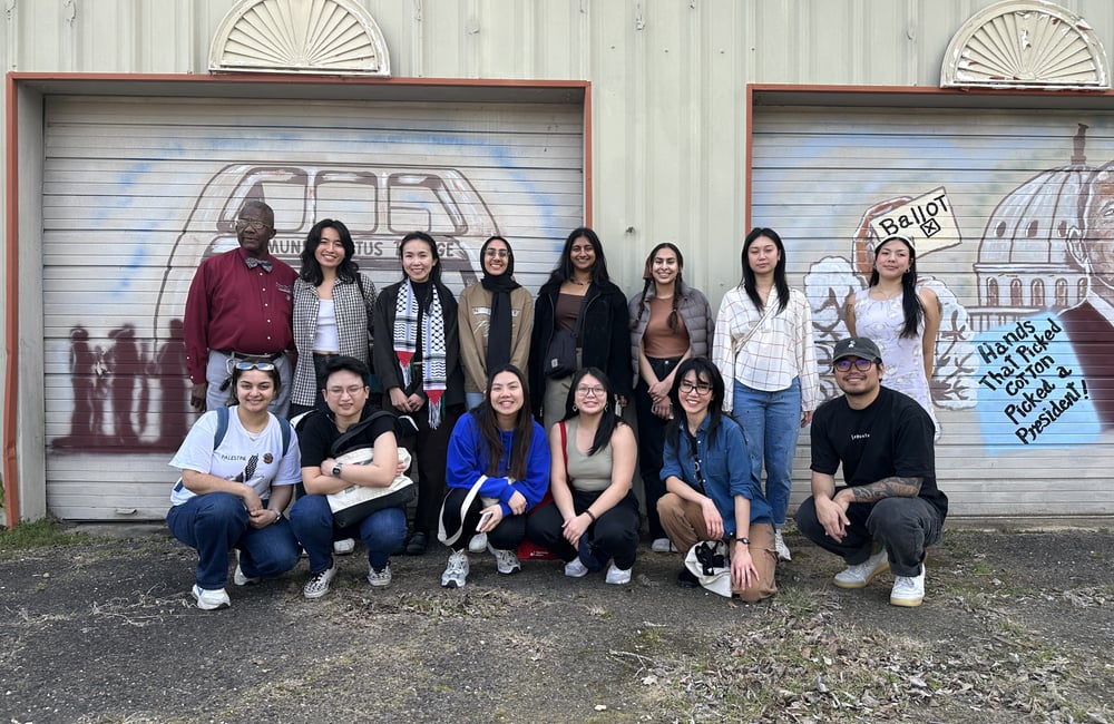 13 staff members pose with tour leader Mr. Jake Williams in front of a Voting Rights mural.
