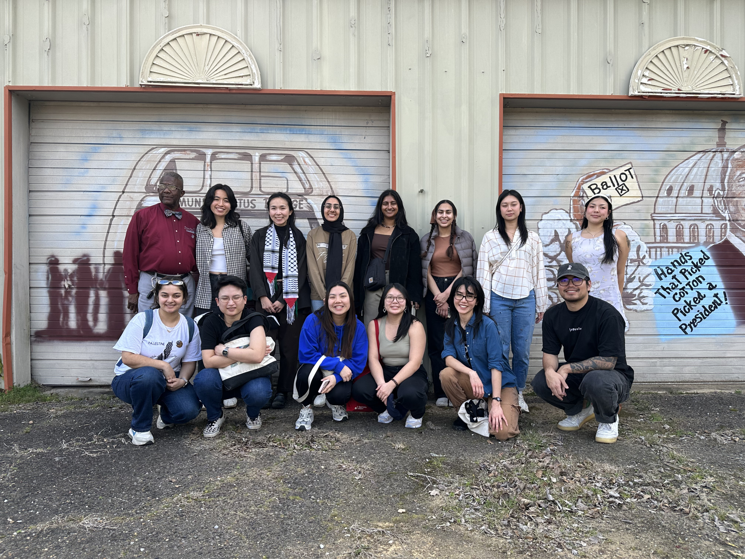 13 staff members pose with tour leader Mr. Jake Williams in front of a Voting Rights mural.