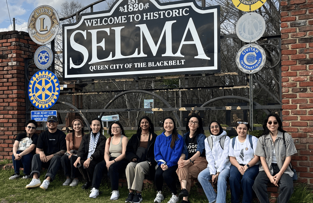 11 staff members pose seated under a sign that reads "Est 1920 Welcome to Historic Selma, Queen City of the Blackbelt"