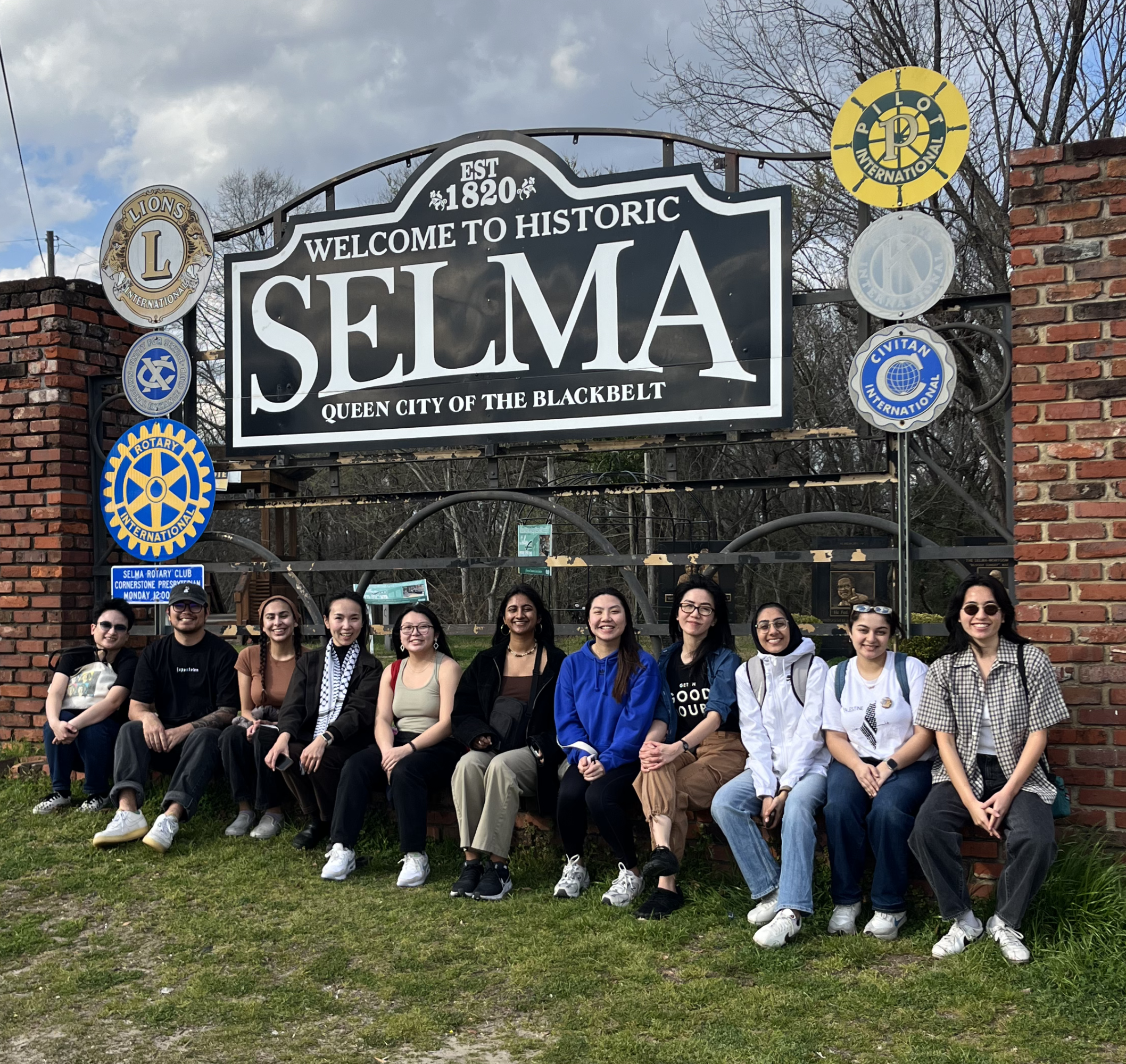 11 staff members pose seated under a sign that reads "Est 1920 Welcome to Historic Selma, Queen City of the Blackbelt"