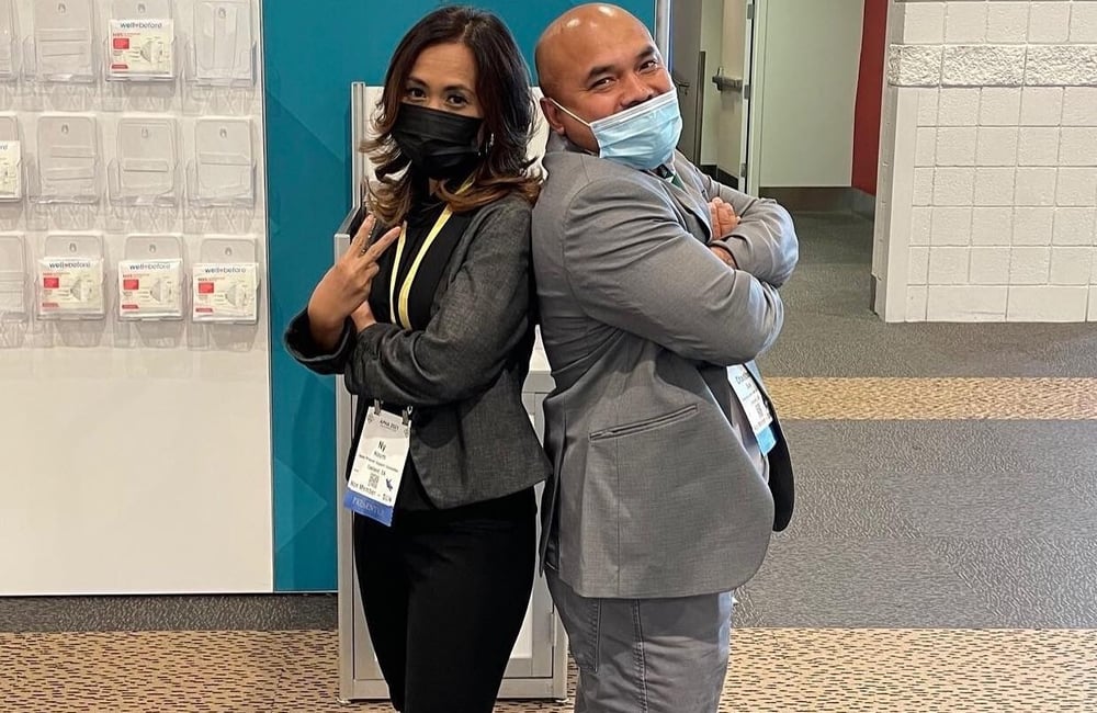Advocates Chanthon Bun and Ny Nourn wearing suits pose back-to-back at a leadership conference.