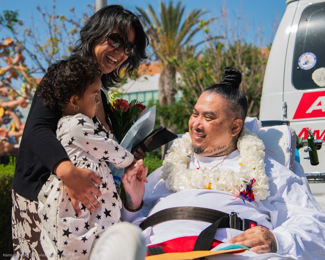 Vithea sits in a stretcher and is greeted by his sister and young niece.
