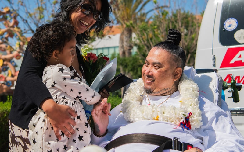 Vithea sits in a stretcher and is greeted by his sister and young niece.
