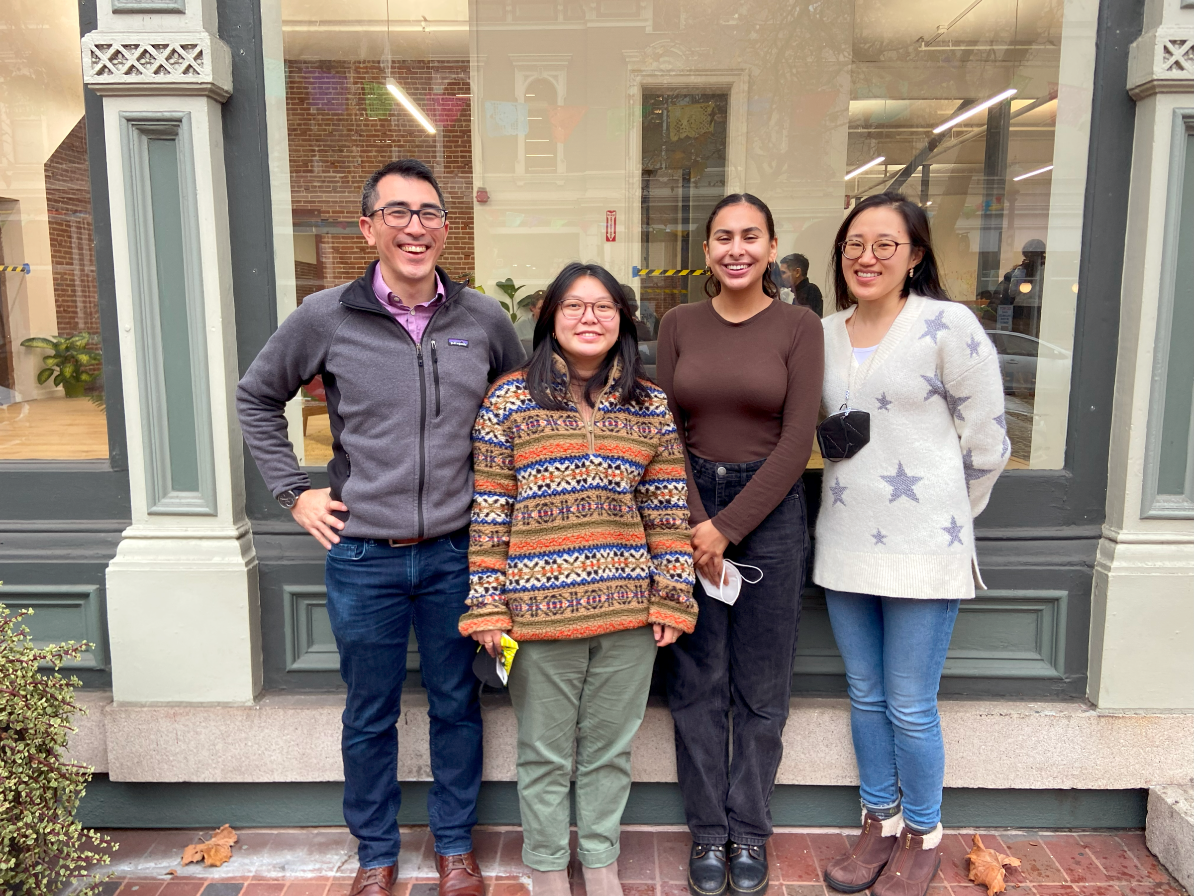 Four people stand pose for a picture outside of a building with decorative molding on its exterior.