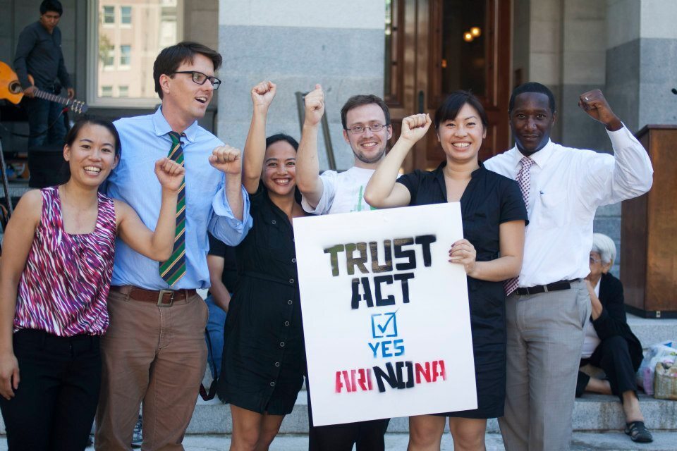 Six people hold up fists and smile, one person is holding a sign that says "Trust Act YES ARINONA"