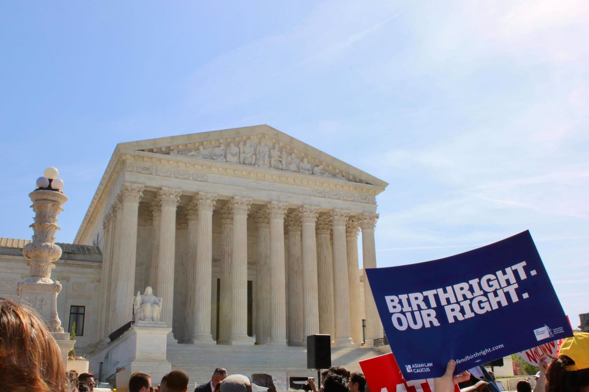 A photo shows the U.S. Supreme Court building in the background. It is a tall, neoclassical stone structure. In the foreground, hands are raised above heads, some holding signs. The most visible sign says, "Birthright. Our Right."
