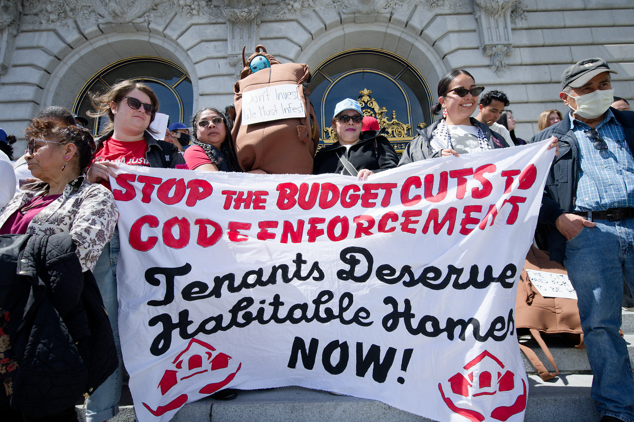 People holding up a sign that reads 'stop the budget cuts to code enforcements. Tenants deserve habitable homes now!'