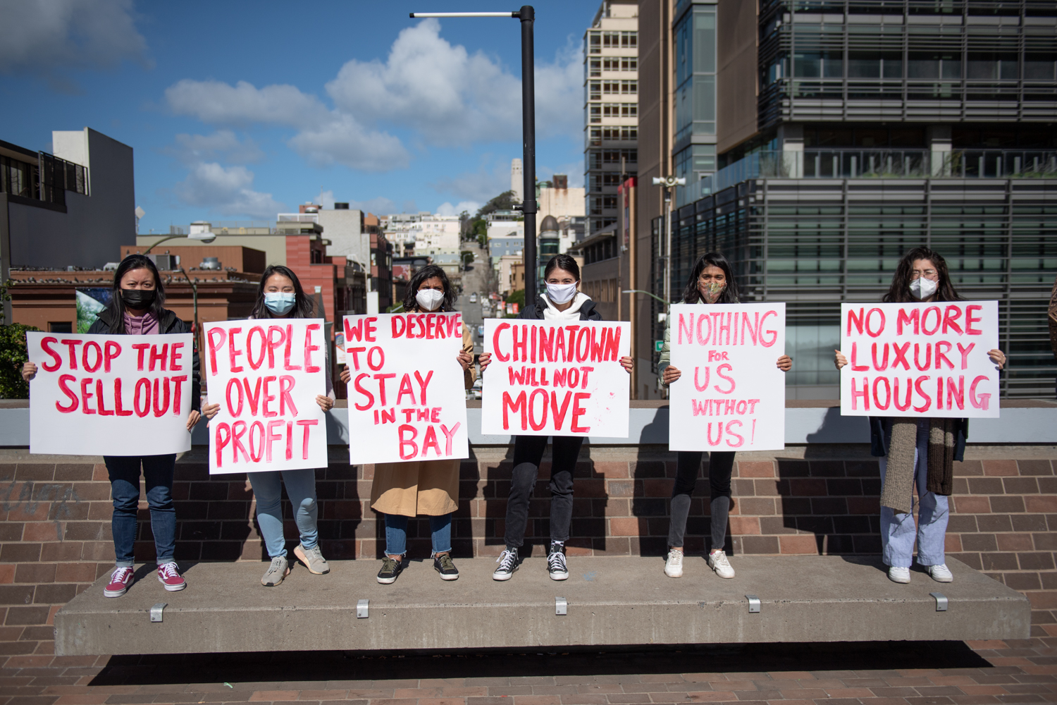 A group of protesters stand lined up holding posters about housing rights.