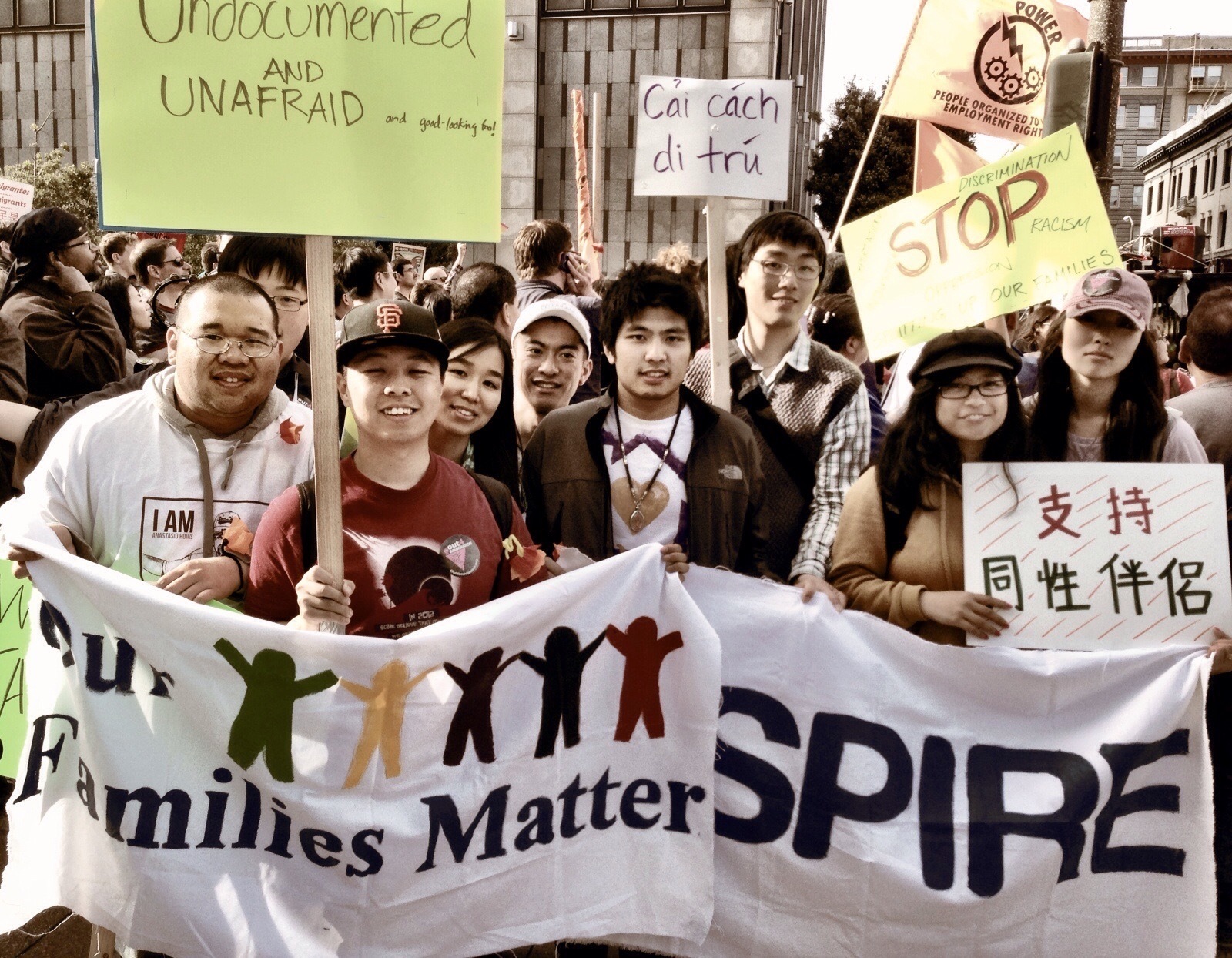 So Young stands in a crowd of protestors holding up banners reading "Families Matter" and "ASPIRE" on a city street.