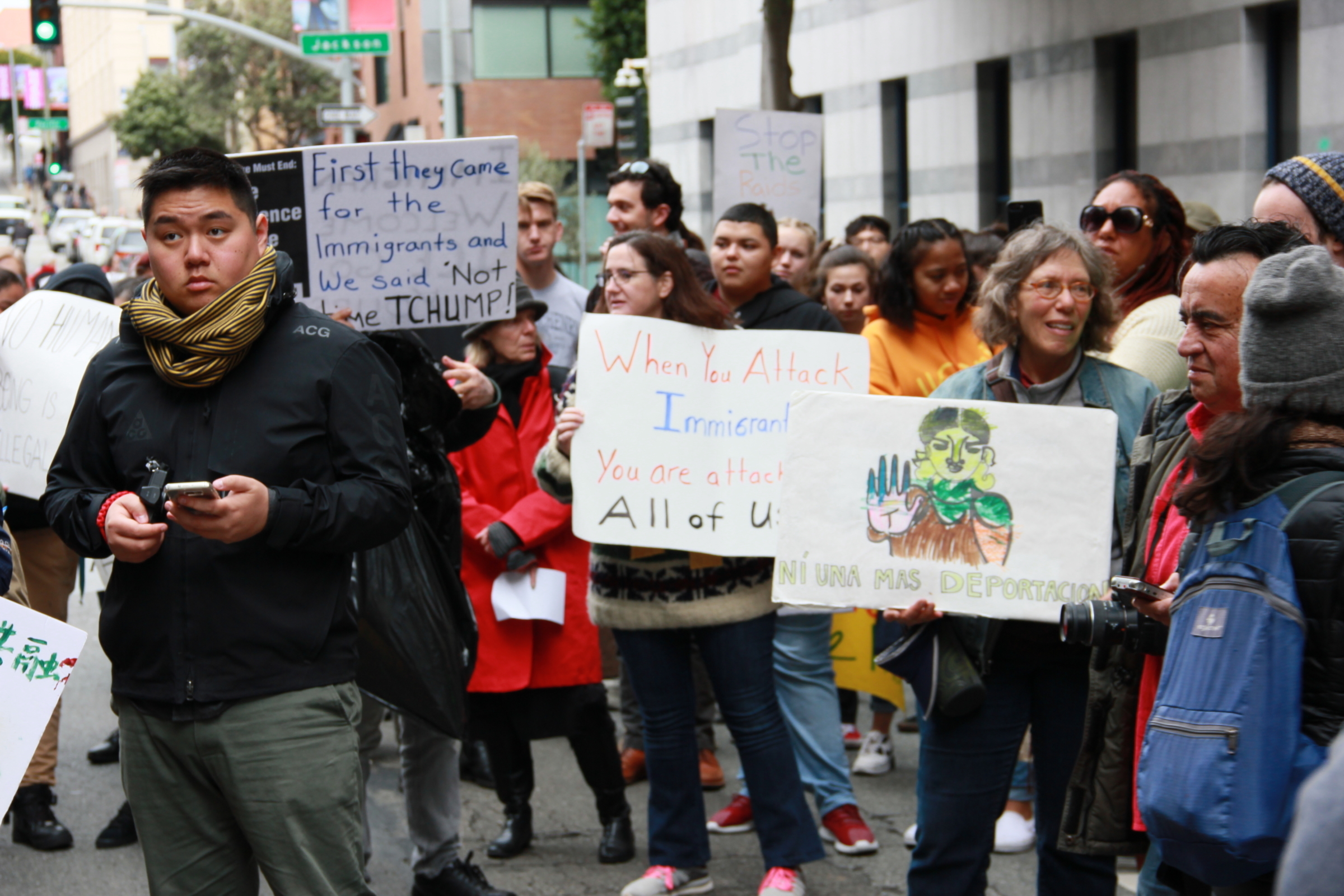 A crowd assembles in the middle of a street outside of the 630 Sansome St ICE office. They hold signs protesting ICE activity.