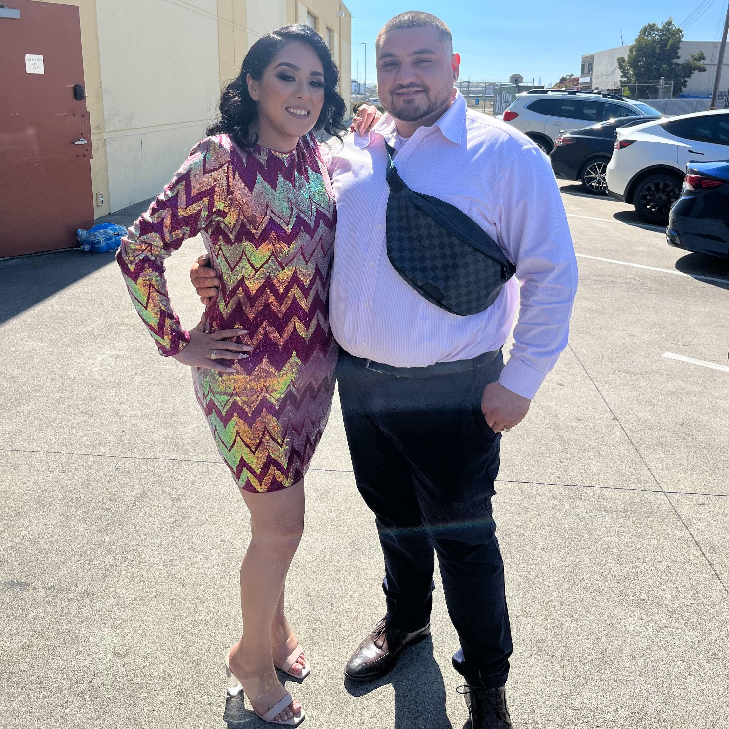 Kassandra and Oscar pose together outside of a building. They wear formal clothing.