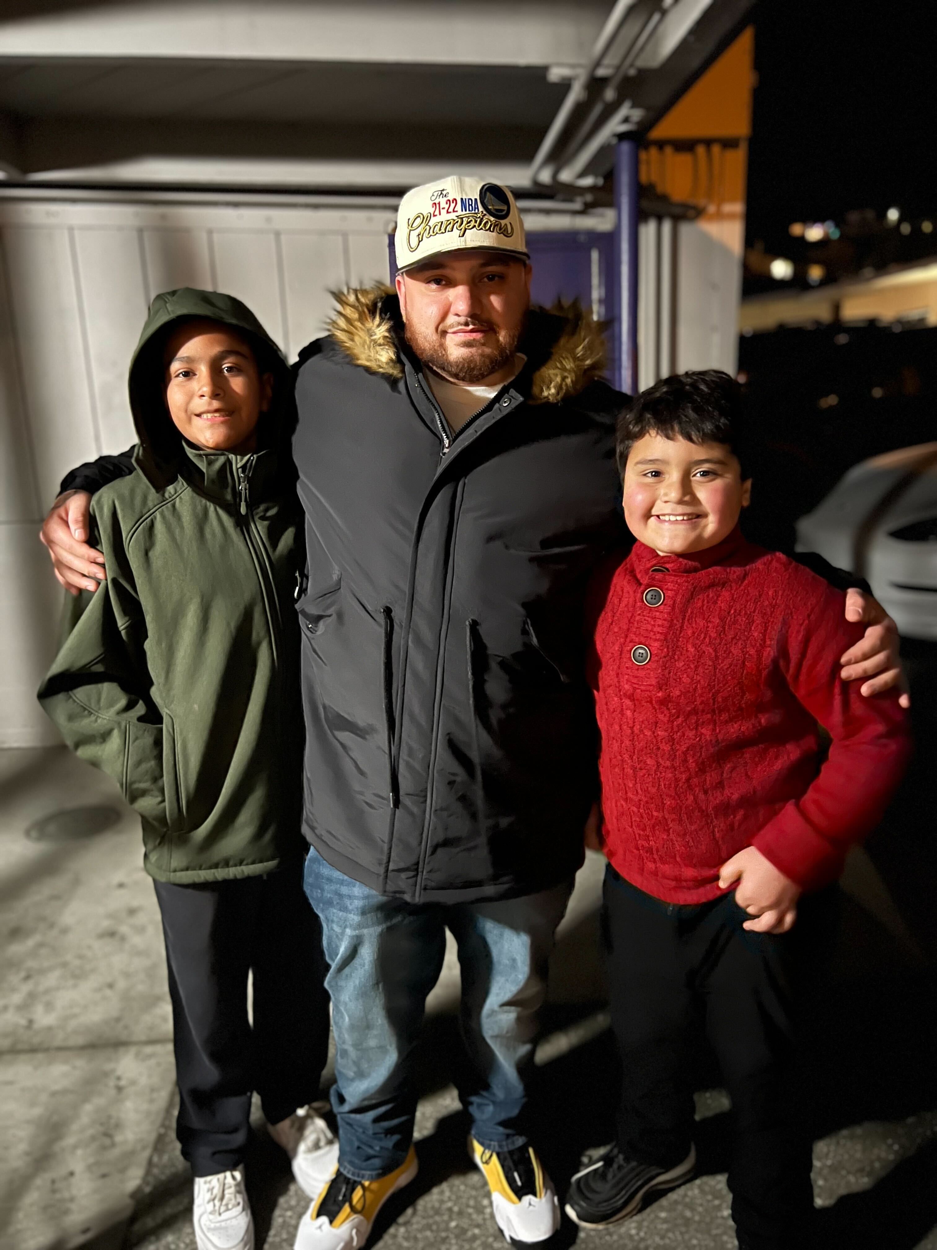 Oscar stands with a boys on either side of him. He hugs them, his hands on their shoulders, as they pose for a photo.