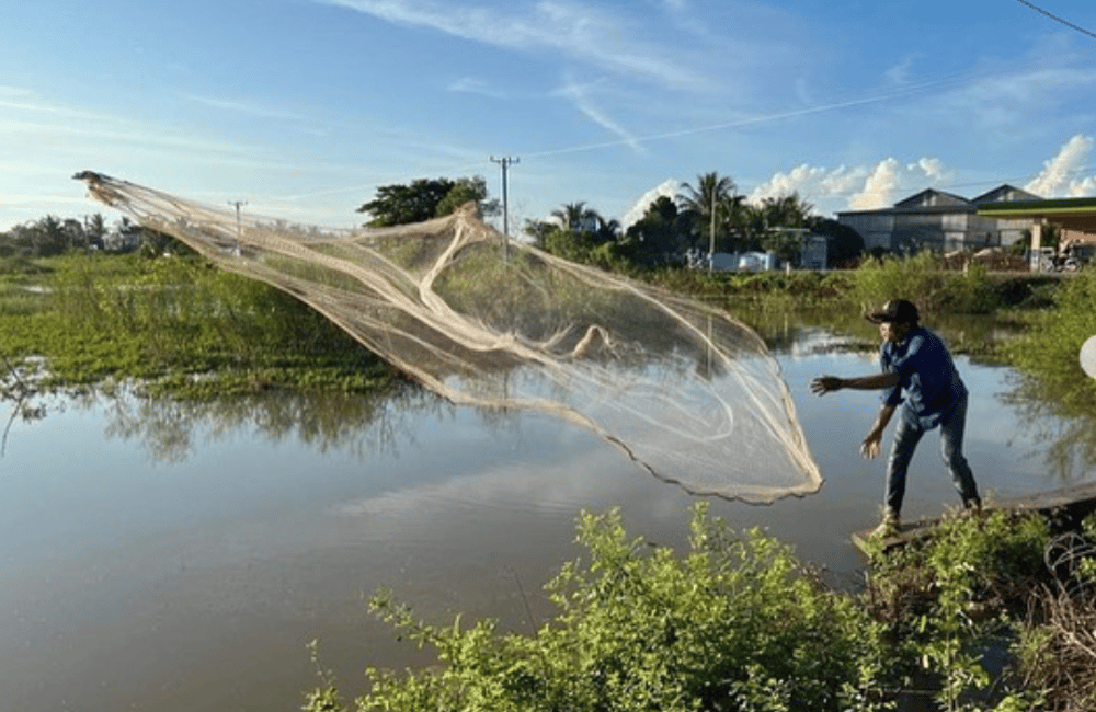 Phoeun throws a fishing net into a lake.
