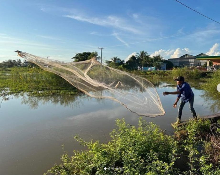 Phoeun throws a fishing net into a lake.