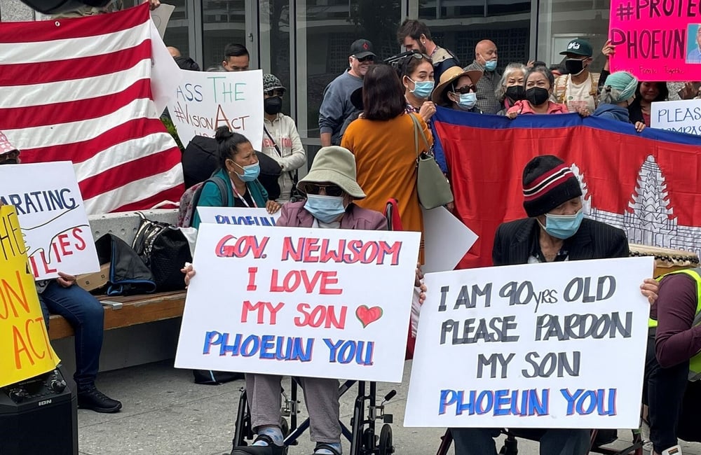 Phoeun You's elderly parents in wheelchairs hold signs at a rally that read "I love my son" "Please pardon my son"