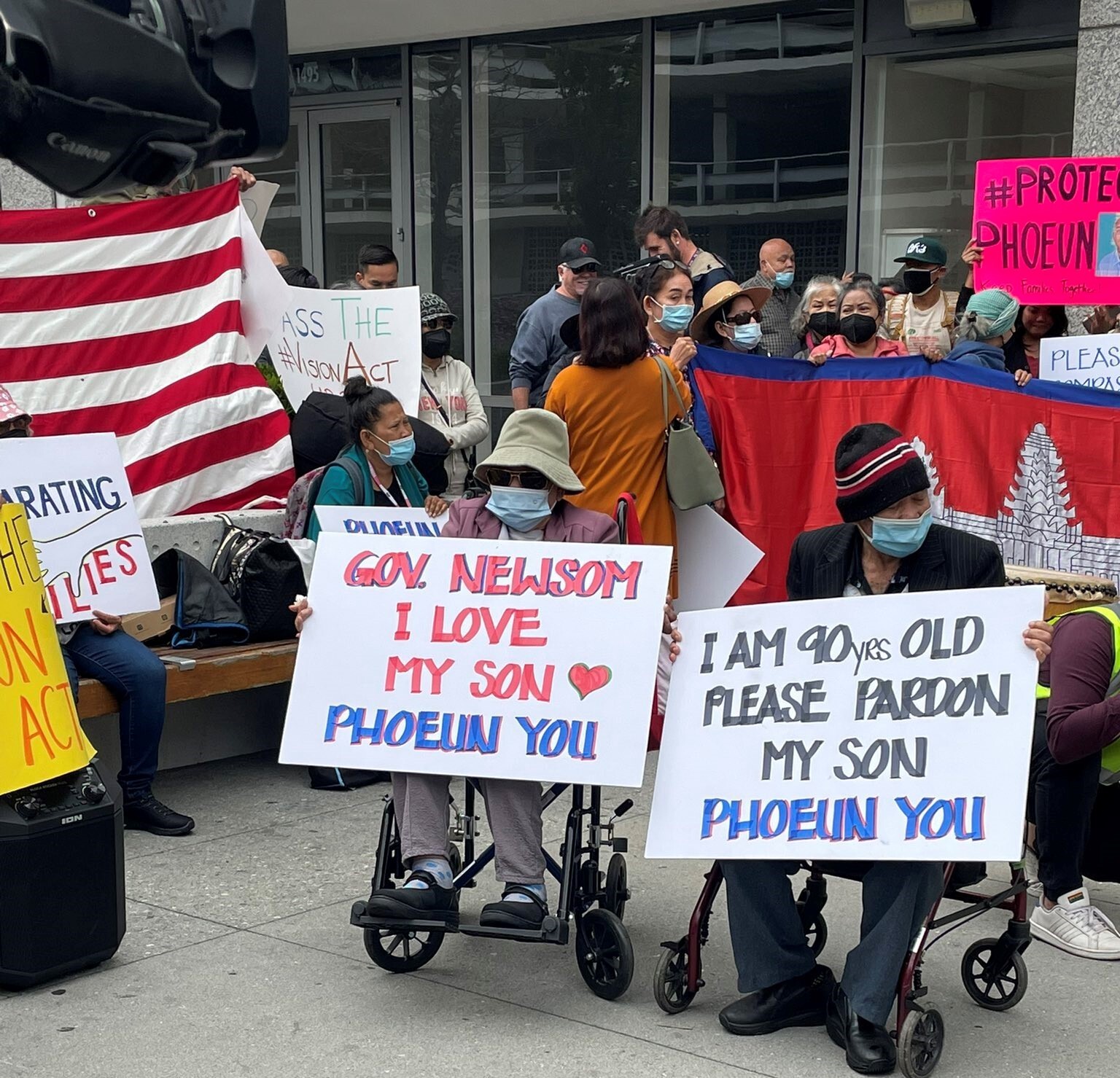 Phoeun You's elderly parents in wheelchairs hold signs at a rally that read "I love my son" "Please pardon my son"