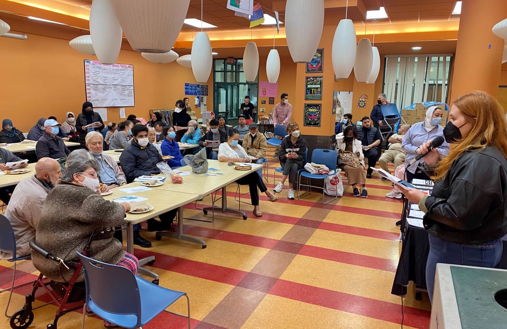 Asian Law Caucus staff member talking on a mic to a room of people sitting at tables at the Chinatown Community Development Center.