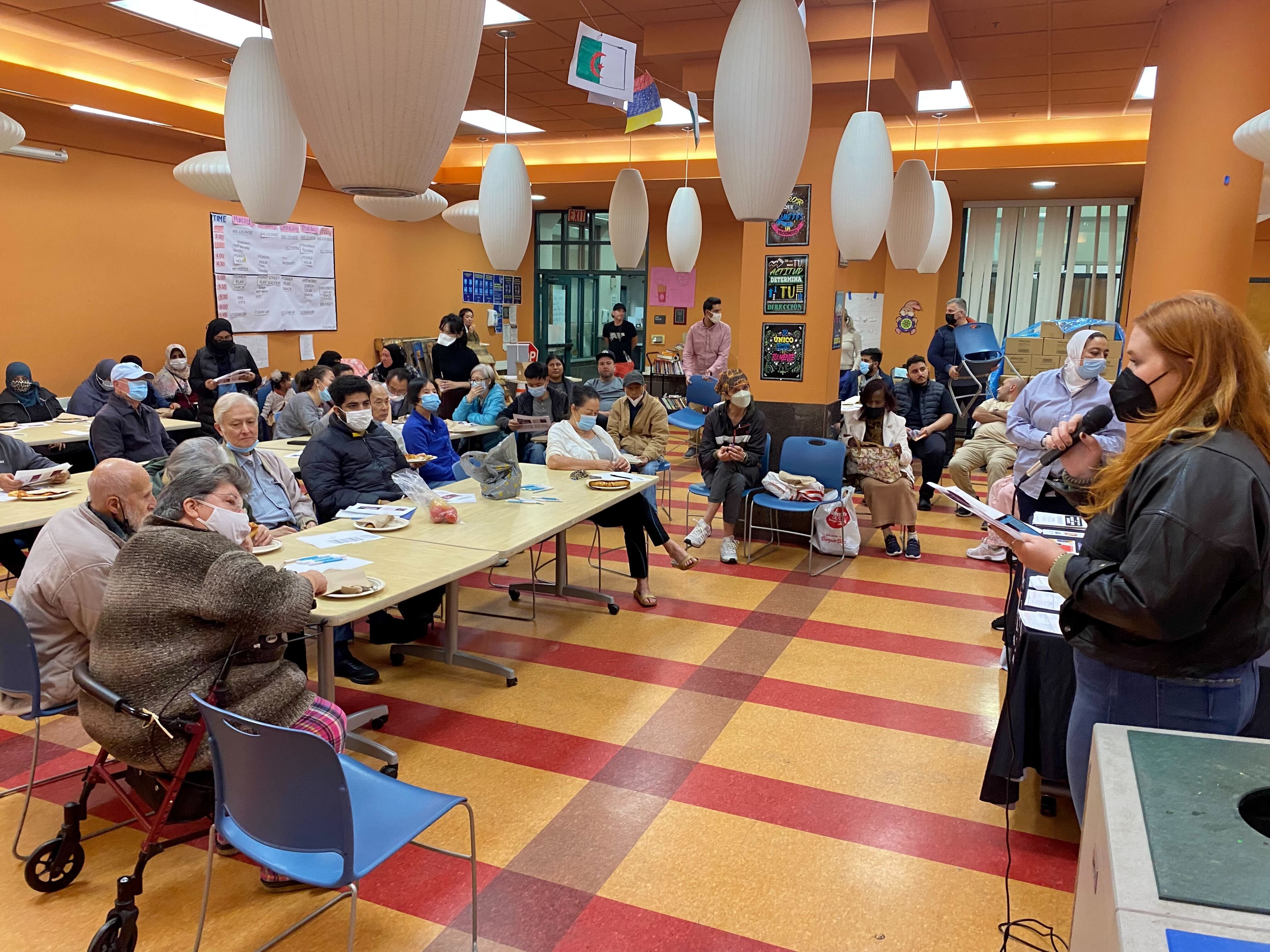 Asian Law Caucus staff member talking on a mic to a room of people sitting at tables at the Chinatown Community Development Center.