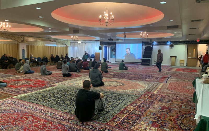 Attendees at the SABA Center are seated on the floor of the mosque listening to a speaker.
