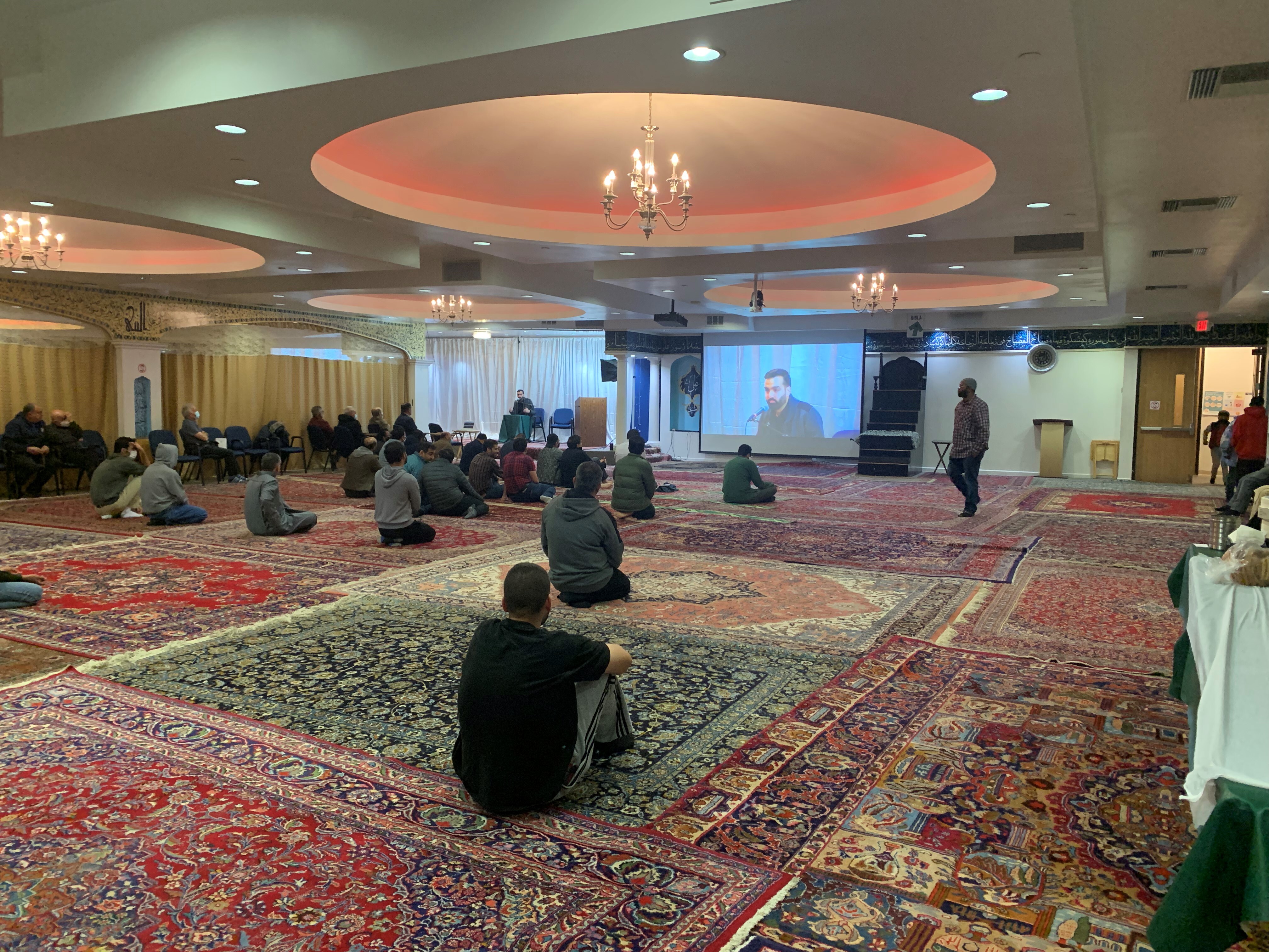 Attendees at the SABA Center are seated on the floor of the mosque listening to a speaker.