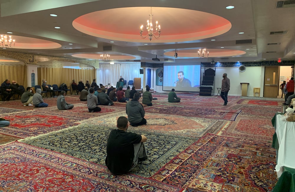 Attendees at the SABA Center are seated on the floor of the mosque listening to a speaker.