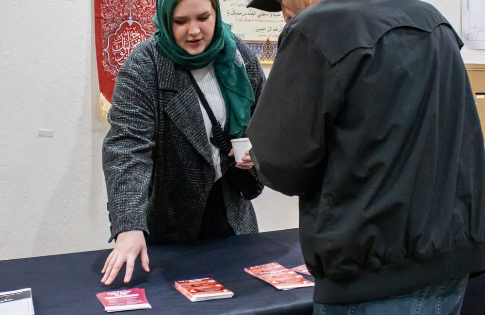 ALC staff member is standing behind the outreach table speaking to a community member about their civil rights and pointing at flyers at SABA Islamic Center. Photo Credit: Jibraan Qureshi