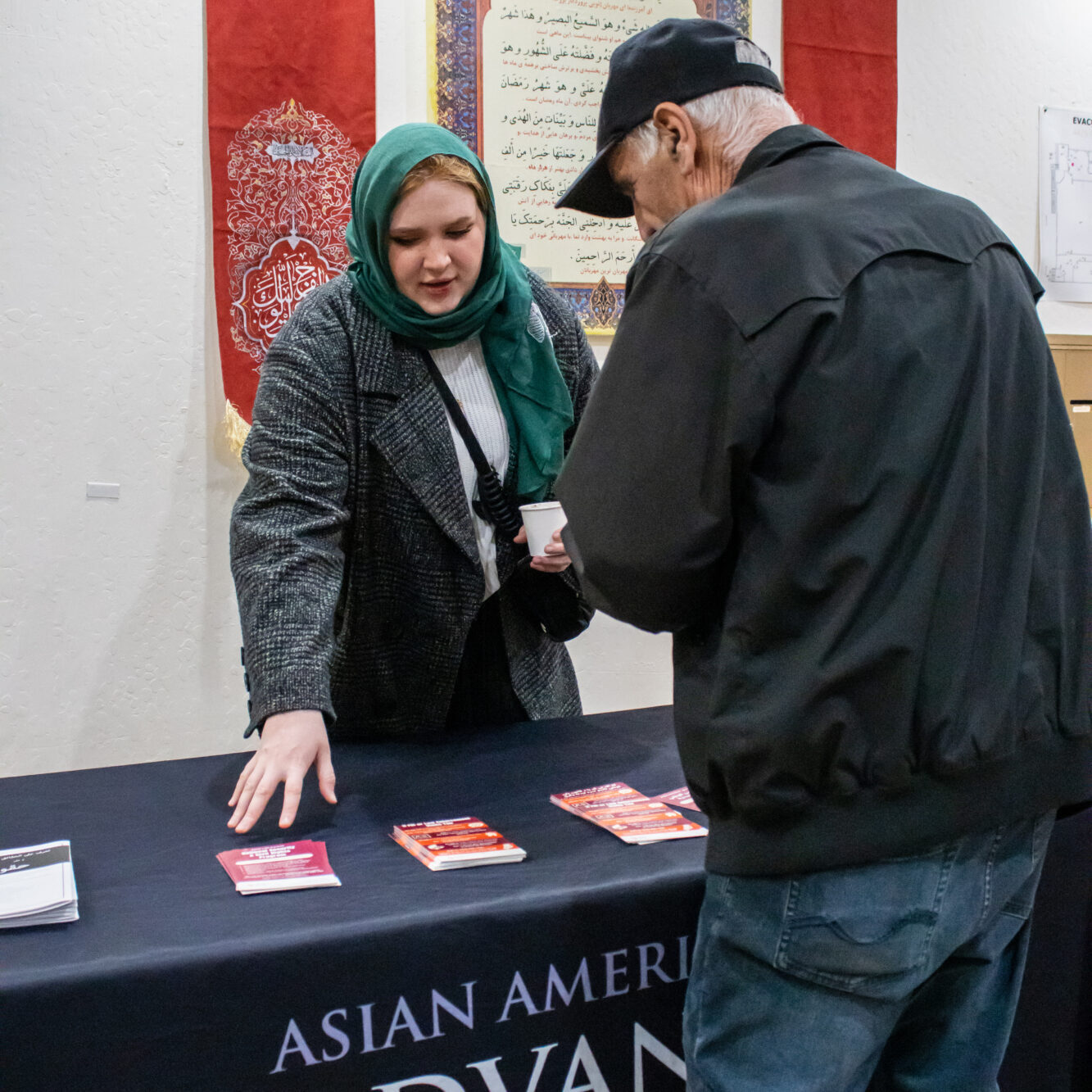 ALC staff member is standing behind the outreach table speaking to a community member about their civil rights and pointing at flyers at SABA Islamic Center. Photo Credit: Jibraan Qureshi