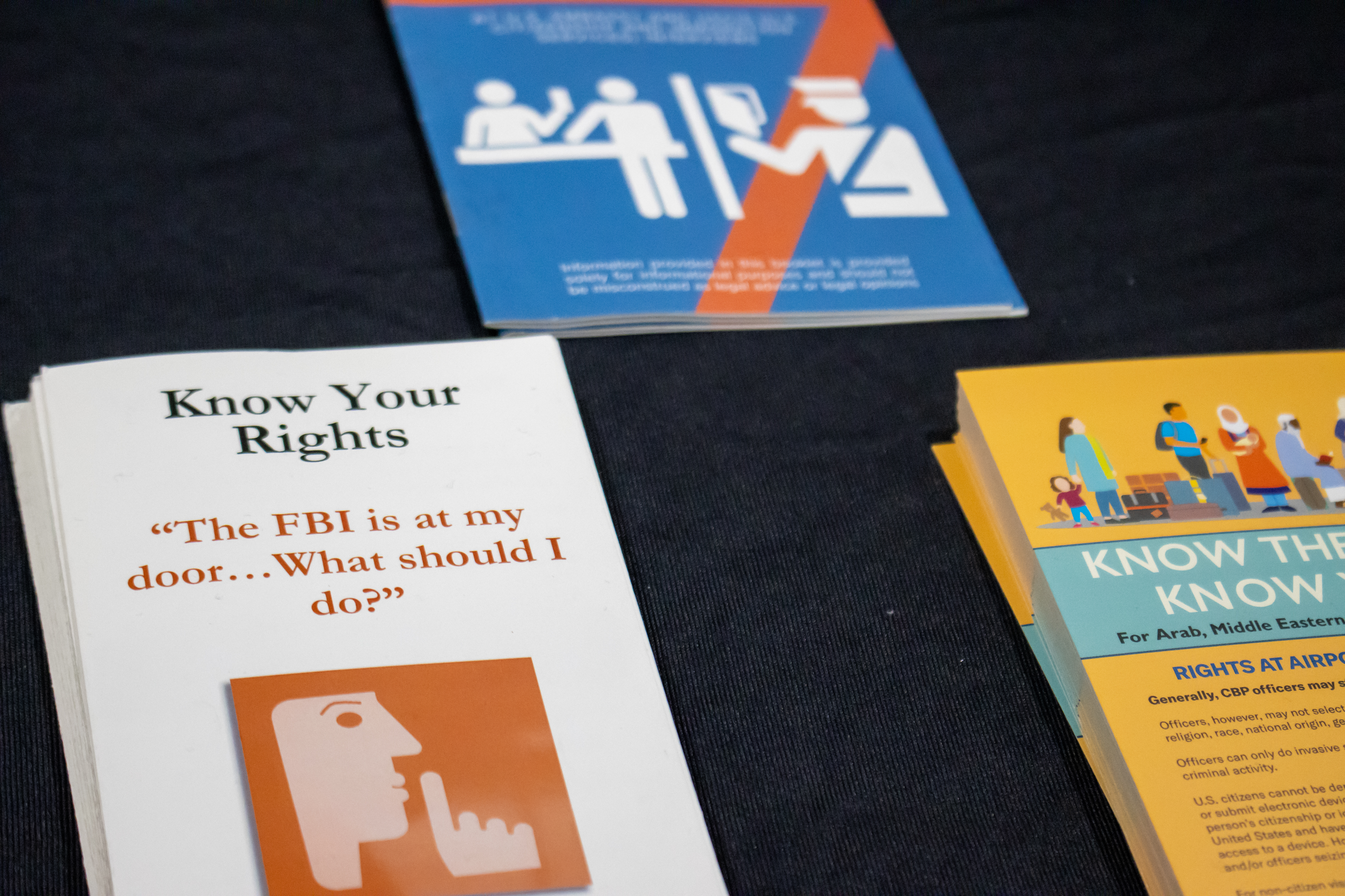 3 different brochures with 'know your rights' information are laid out on a table with a black background.