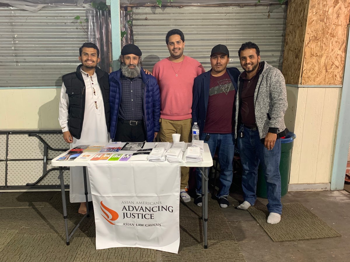 Two Asian Law Caucus staff and three Bay Area community members stand together behind a table with know-your-rights materials and a white banner with the ALC logo on it.