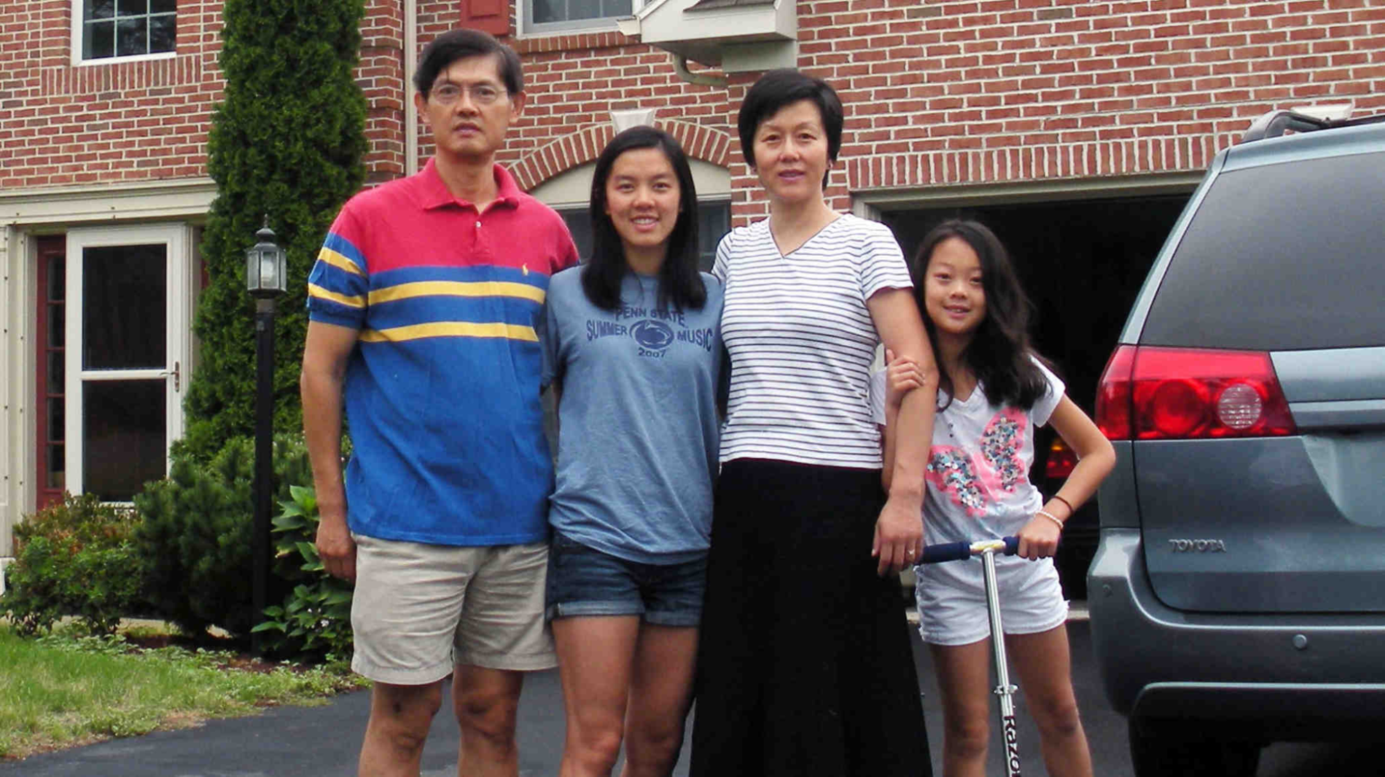 Professor Xi stands with his wife and two young daughters in front of their home.