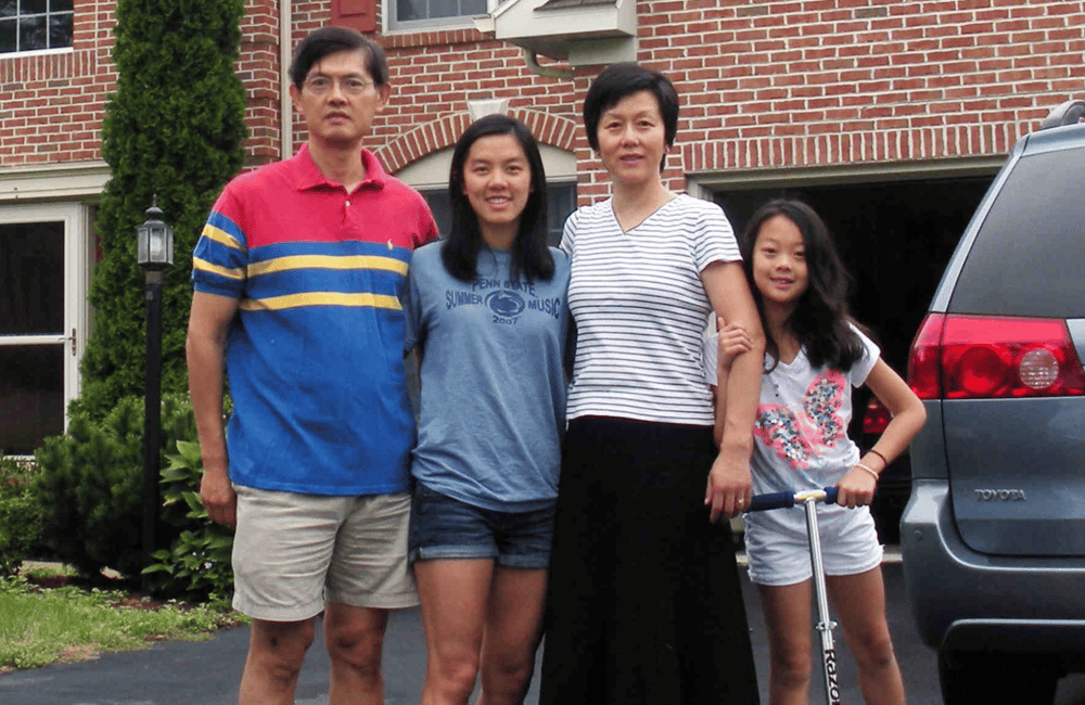 Professor Xi stands with his wife and two young daughters in front of their home.