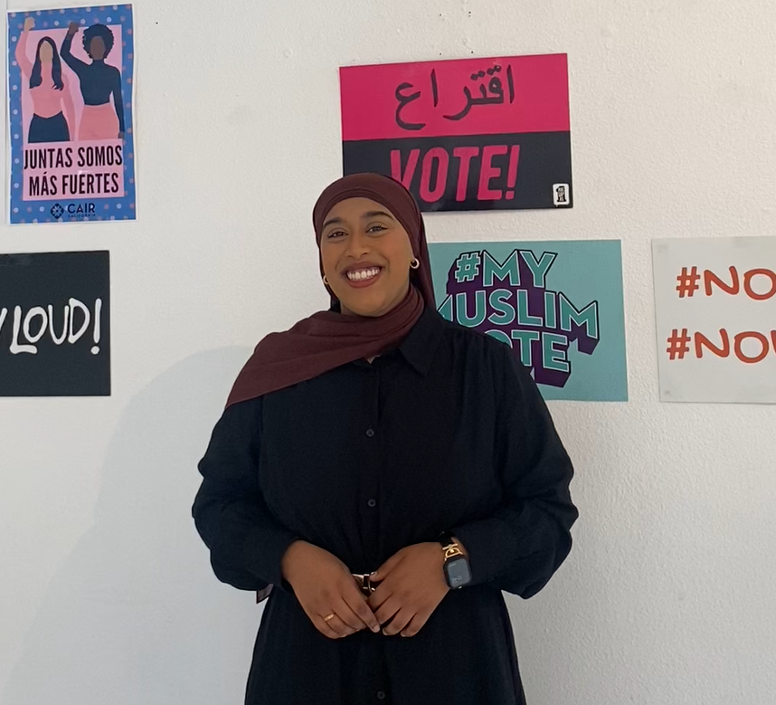 Fauziya poses in front of a wall with voting signs.