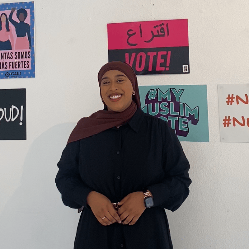 Fauziya poses in front of a wall with voting signs.