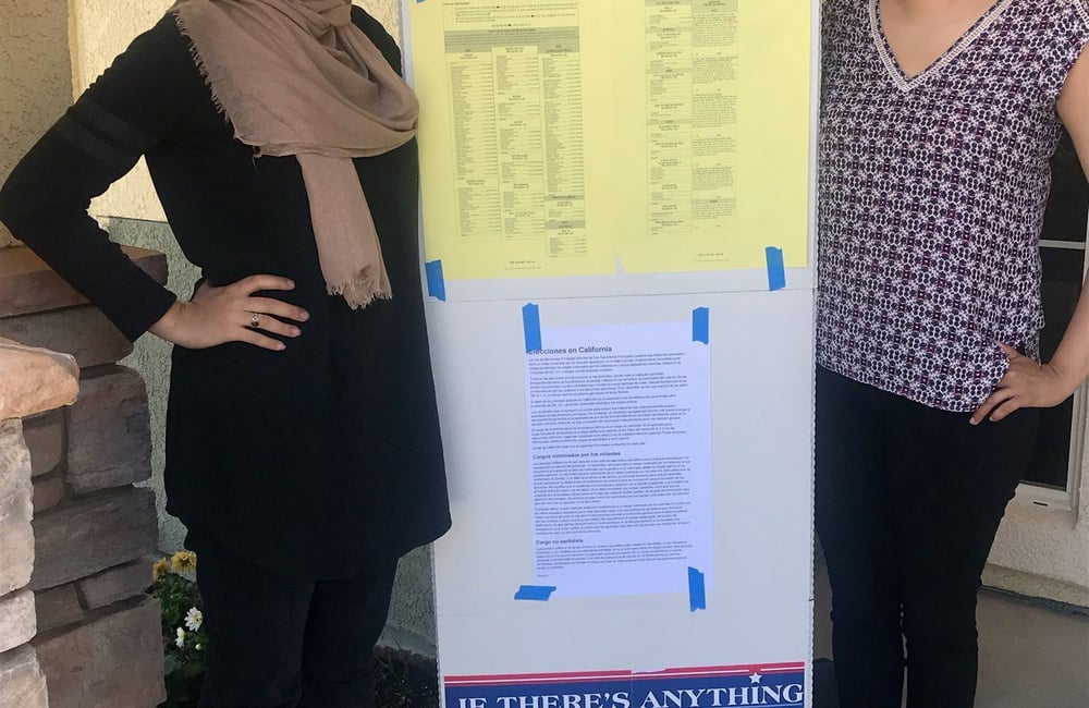 Two women stand with a sign between them at a polling location