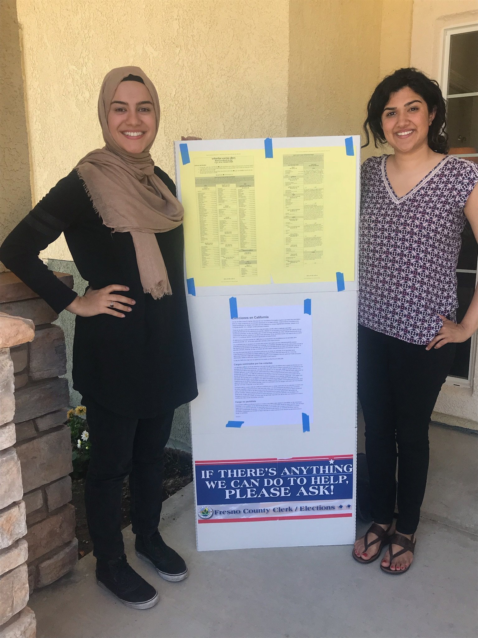 Two women stand with a sign between them at a polling location