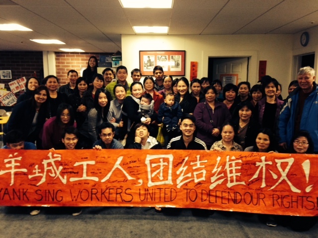 A group of people stand in front of a banner reading ""Yank Sing Workers Untied to Defend our Rights" in English and Chinese